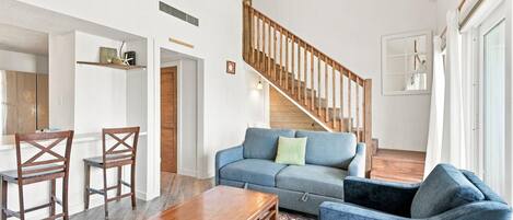 A spacious living area with a wooden staircase, a blue sofa, a wooden coffee table, and a patterned rug.
