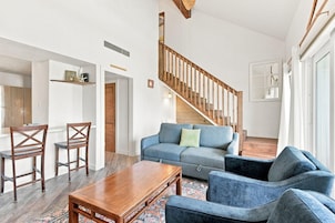 A spacious living area with a wooden staircase, a blue sofa, a wooden coffee table, and a patterned rug.