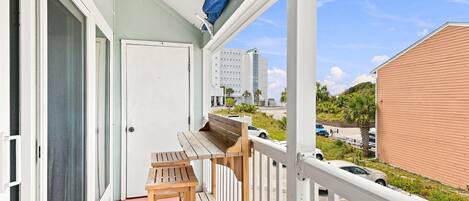 A balcony with a wooden table and chairs, a white door, and a view of a building and parked cars.
