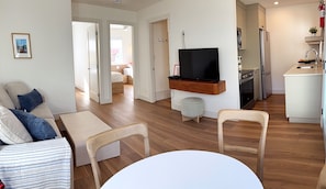Una sala de estar moderna con sofá, sillas, televisor y mesa de comedor.
