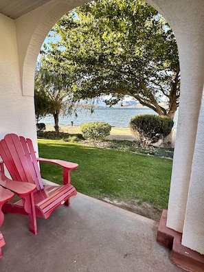 A red Adirondack chair on a concrete patio with a view of a lake and mountains.