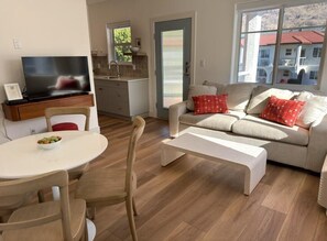 A modern living room with a sofa, a coffee table, a TV on a stand, and a dining area with a table and chairs.