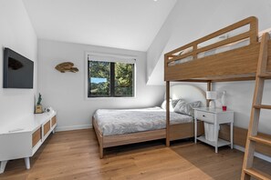 A bedroom with a bunk bed, a desk, a chair, a window with a view of greenery, and a mounted television. - Black House Red Roof - Langs Beach Holiday Home (Langs Beach)