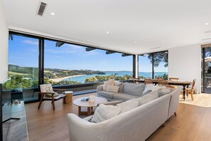 A modern living room with a large sofa, a coffee table, and a dining area with chairs and a table. - Black House Red Roof - Langs Beach Holiday Home (Langs Beach)