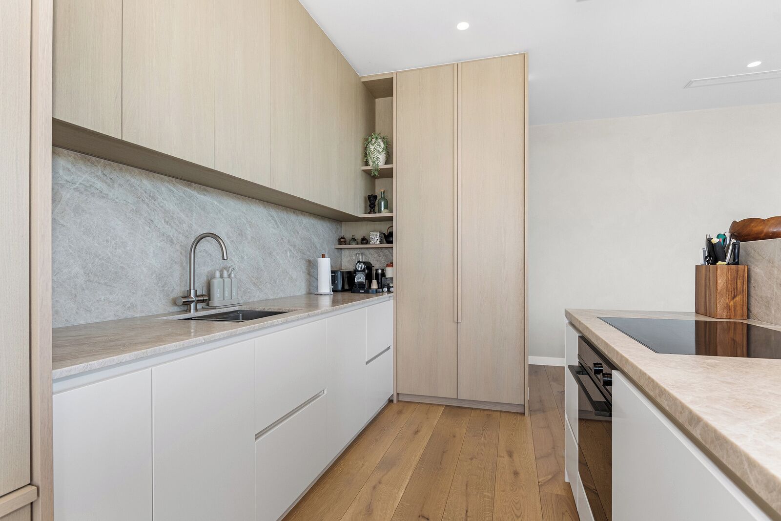 A modern kitchen with white cabinetry, a marble backsplash, and a wooden floor.