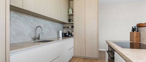 A modern kitchen with white cabinetry, a marble backsplash, and a wooden floor.