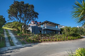 A modern two-story house with a flat roof, large windows, and a well-maintained garden with various plants. - Black House Red Roof - Langs Beach Holiday Home (Langs Beach)