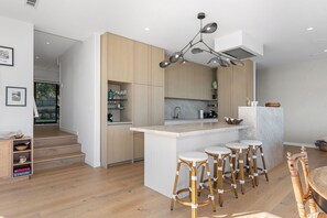 A modern kitchen with a central island, bar stools, and a dining area. - Black House Red Roof - Langs Beach Holiday Home (Langs Beach)