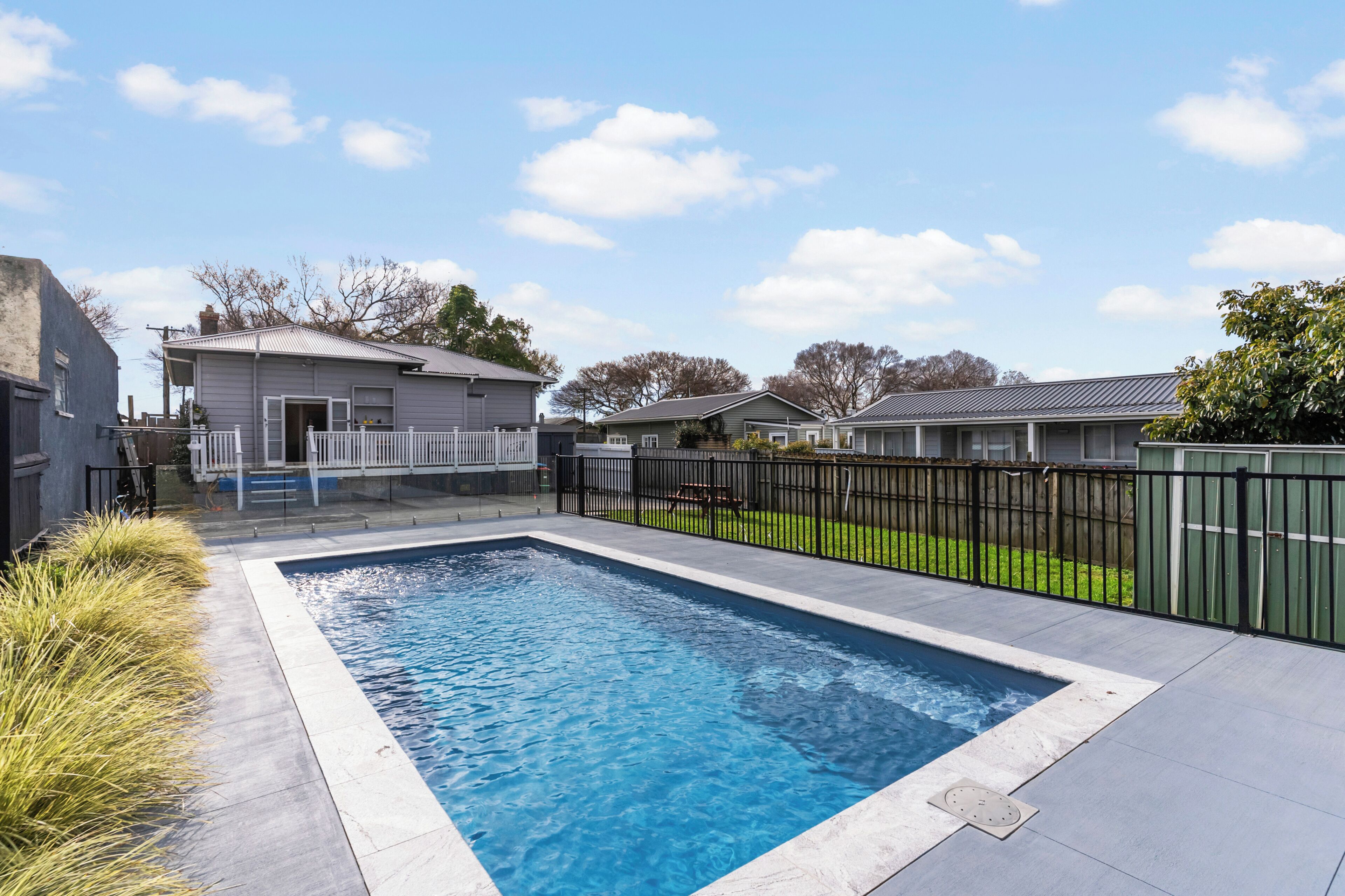 Una piscina rectangular amb un marc blanc, envoltada per un terra enrajolat.