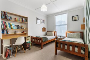 A bedroom with two wooden beds, a desk with a chair, a bookshelf, and a window. - Poolside Pause - Auckland Holiday Home (Auckland)