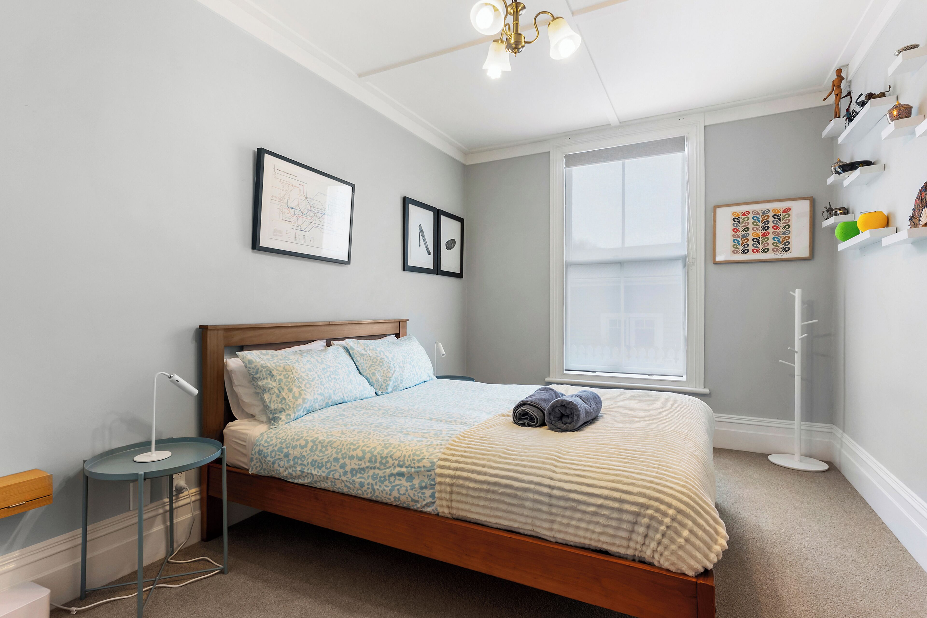 A neatly arranged bedroom with a bed, bedside table, lamp, and wall-mounted shelves.