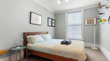 A neatly arranged bedroom with a bed, bedside table, lamp, and wall-mounted shelves.
