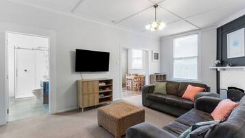 A modern living room with a flat-screen TV, a sofa set, a wicker ottoman, and a dining area with a table and chairs.