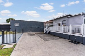 A residential property with a concrete driveway, a white fence, and a grey building with a visible garage door. - Poolside Pause - Auckland Holiday Home (Auckland)