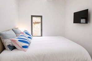 Ein Schlafzimmer mit einem großen Bett, einem Fenster und einem an der Wand befestigten Fernseher.