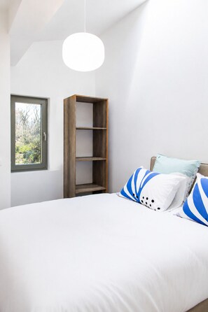Ein Schlafzimmer mit einem Bett, einem Holzregal und einem Fenster.