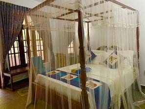 Uma cama de dossel com cortina, um banco de madeira e uma janela com cortinas.