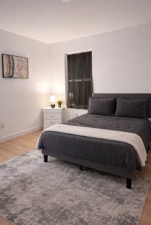 A bedroom with a bed, bedside table, lamp, and a painting on the wall. - Exotic Escapes | Modern Spacious 3BR Near Downtown (Houston)