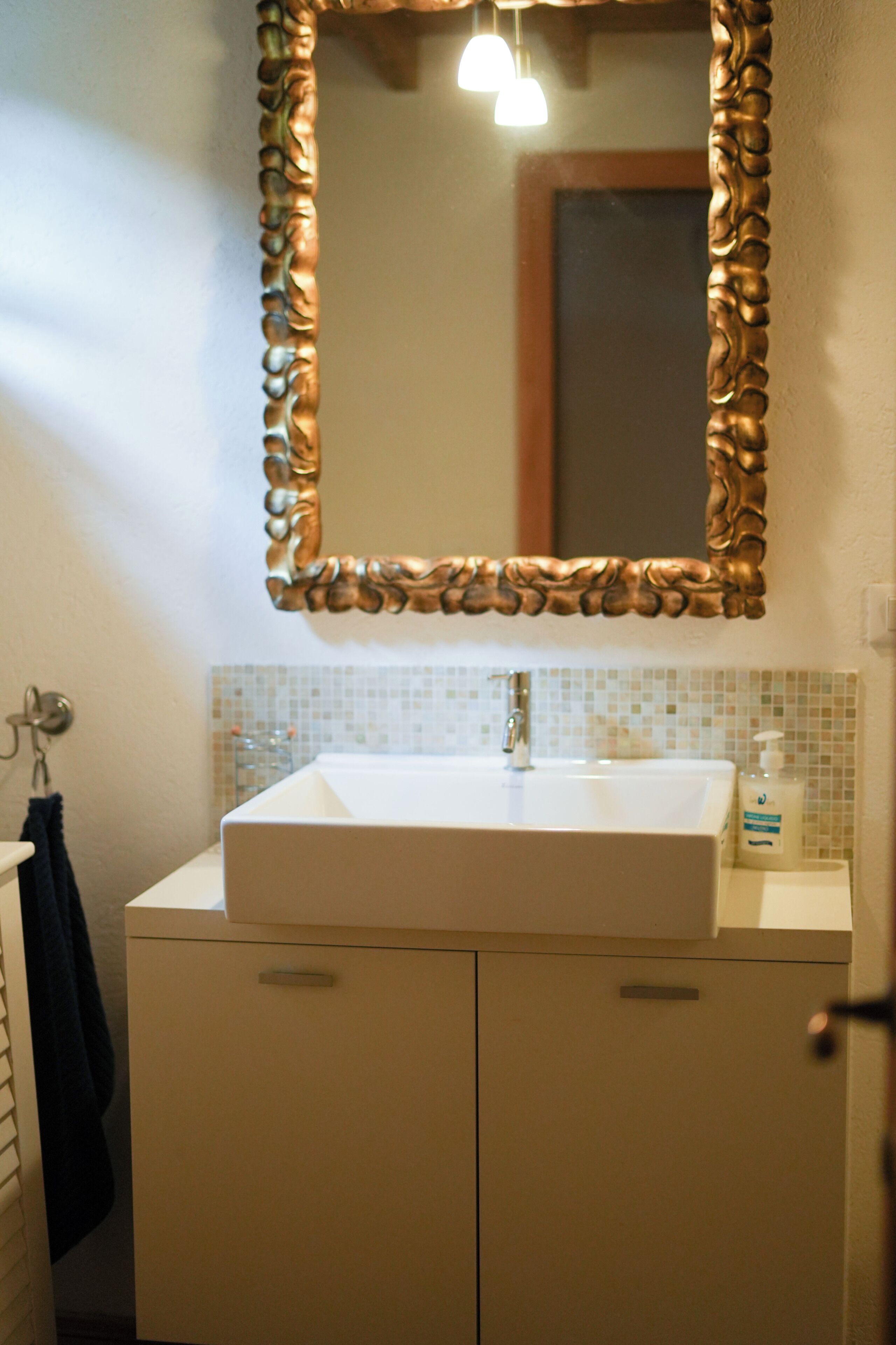 A bathroom with a white sink, a mirror with a decorative frame, and a tiled backsplash.