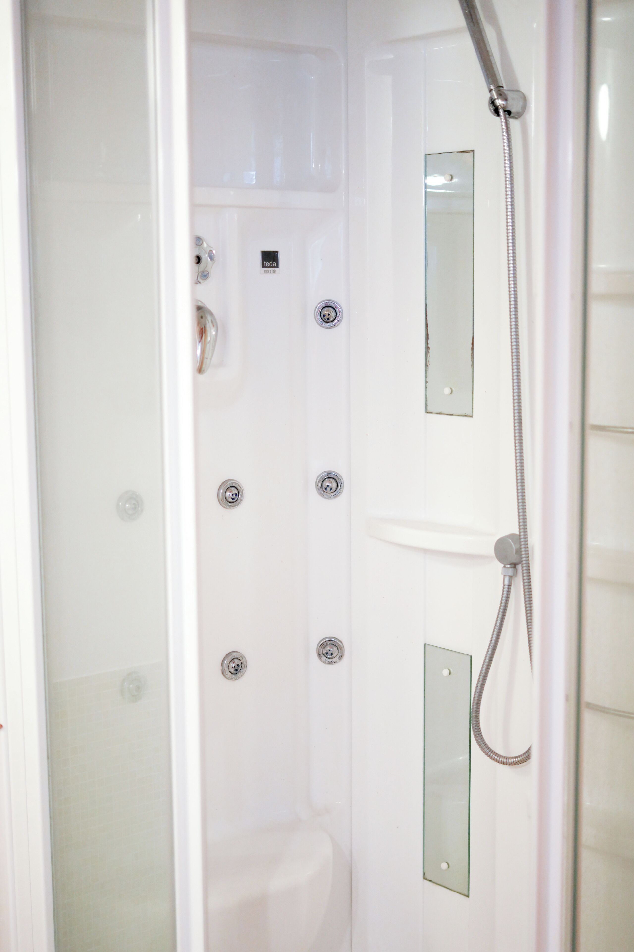 Ein helles Badezimmer mit Glasdusche, Handbrause und Spiegel.
