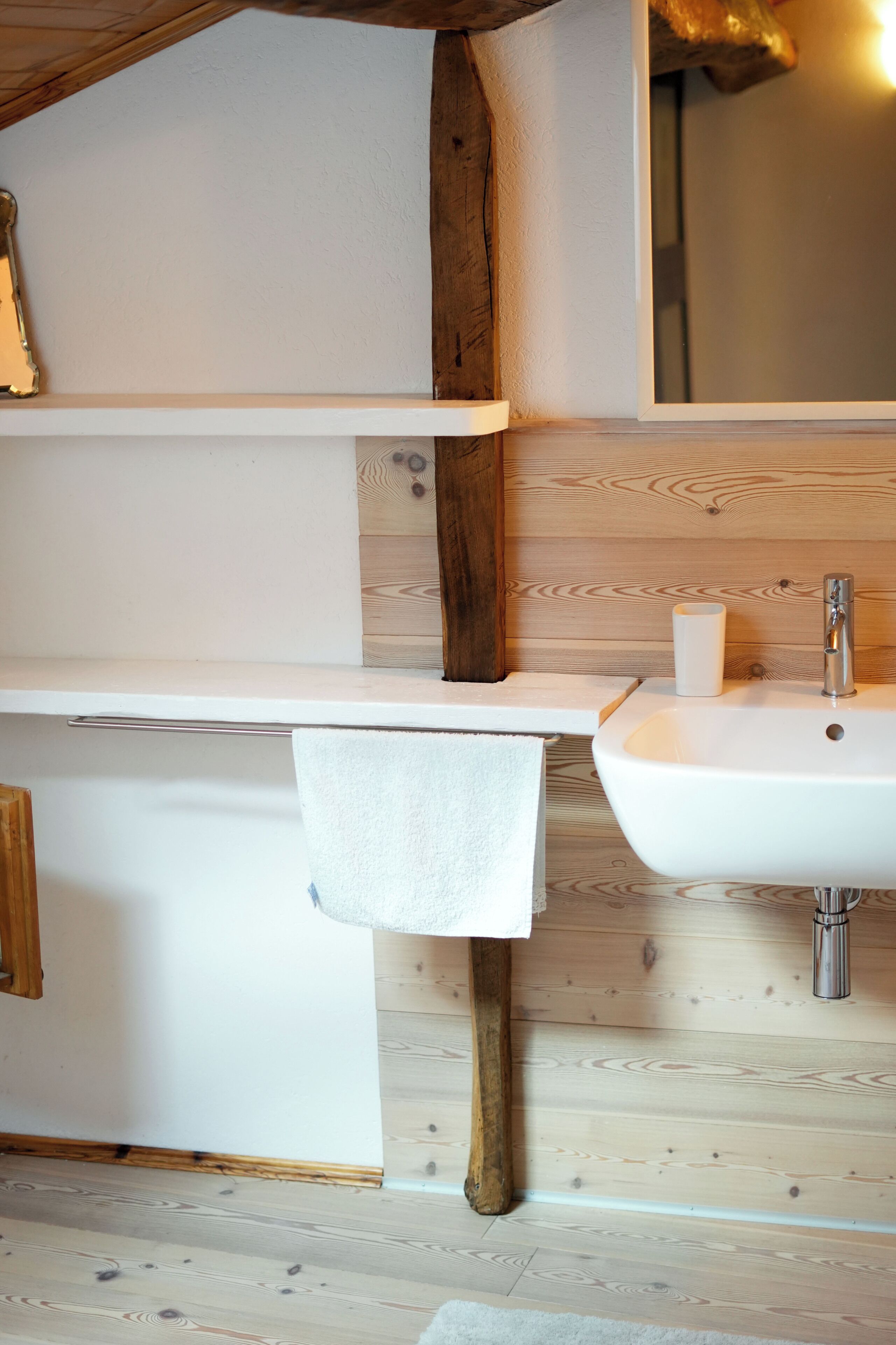A bathroom with a wooden floor, a white sink, and a mirror above the sink.