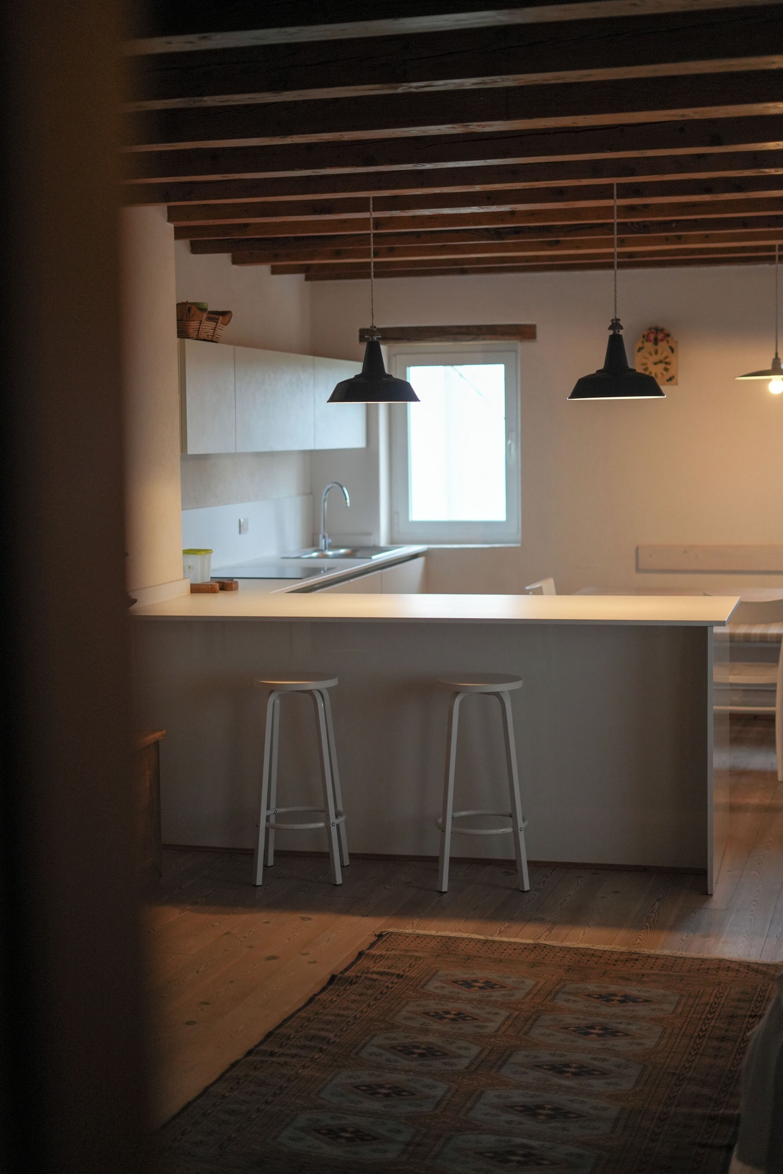 Une cuisine moderne dotée d’un grand îlot central, de deux tabourets de bar, d’un éclairage suspendu et d’une fenêtre.