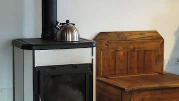 A wood-burning stove with a kettle on top, a wooden chest, and a painting on the wall.