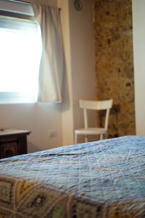 A bed with a patterned bedspread, a chair, and a window with curtains.