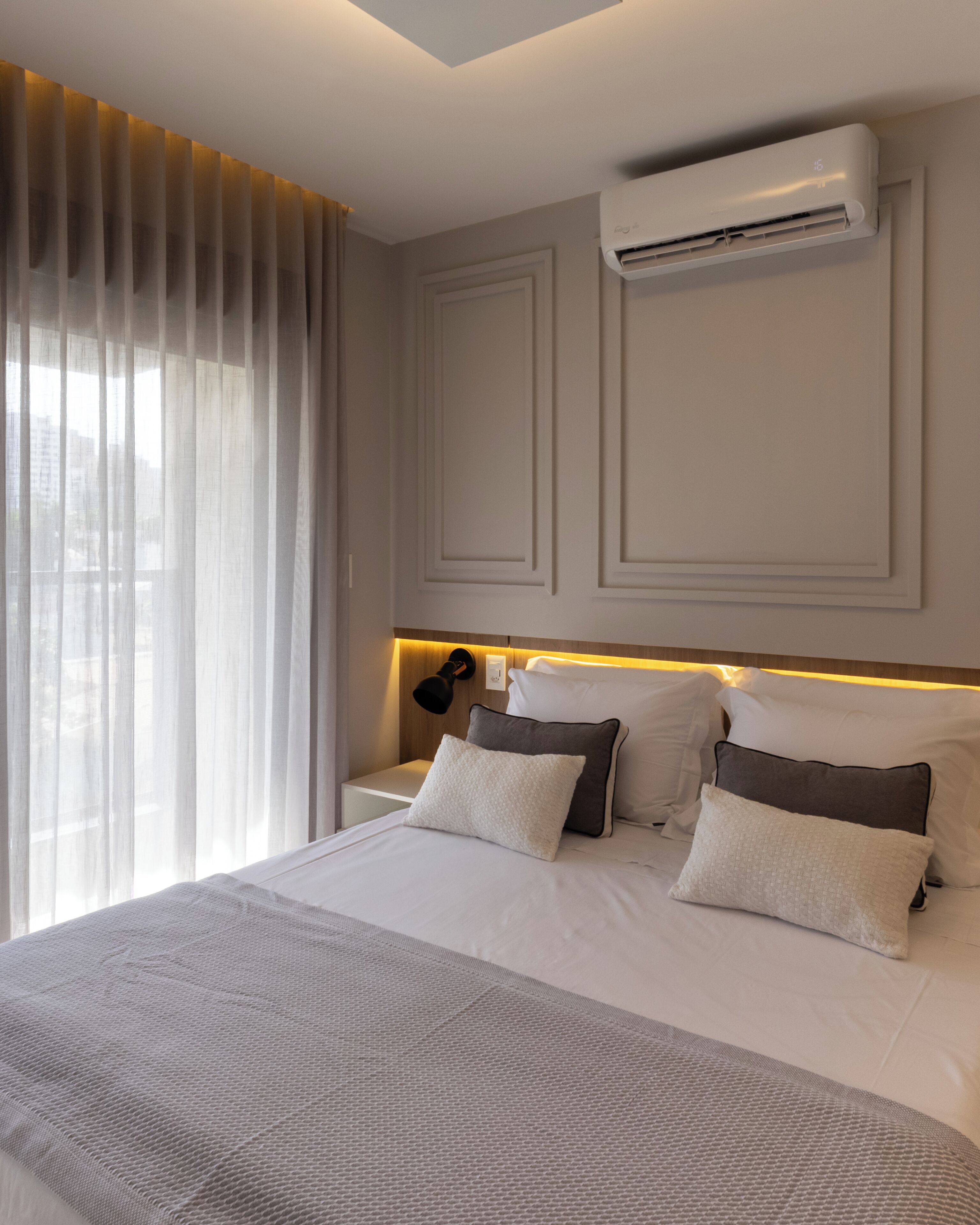 Habitación de hotel con cama, mesita de noche, equipo de aire acondicionado y ventana con cortinas.