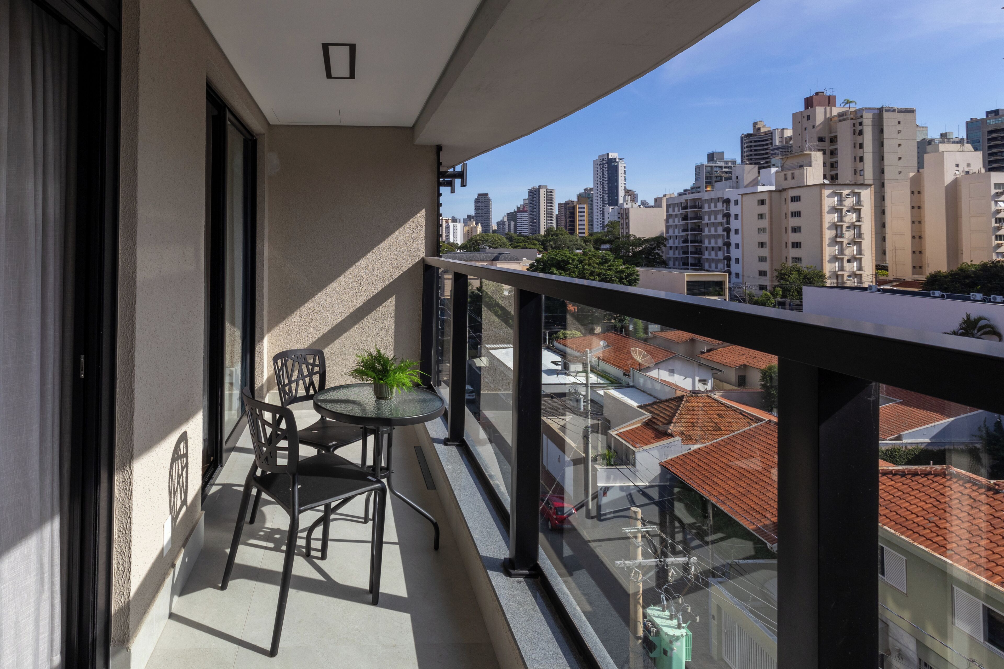 Un balcón con mesa y sillas, con vista a un paisaje urbano que incluye varios edificios.