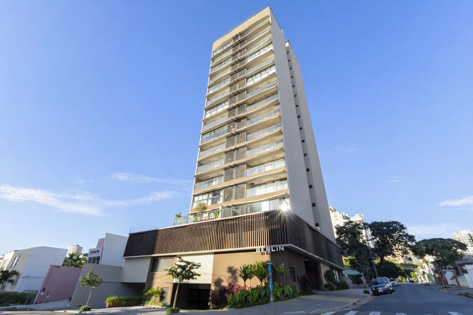 A modern high-rise building with multiple balconies, a flat facade, and a clear sky.