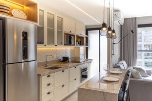 Uma cozinha moderna com eletrodomésticos de aço inoxidável, bancada de mármore e área de refeições com sofá e mesa.