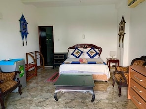 A bedroom with a bed, bedside tables, a desk, a chair, a dresser, and a clock on the wall.