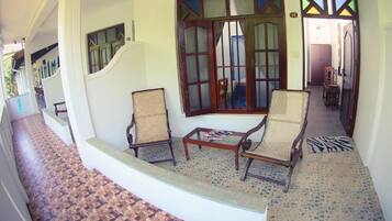 Un pasillo con una escalera que lleva a una habitación con dos sillas de mimbre, una mesita y un ventanal con un marco decorativo.