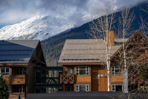 A mountain lodge with a wooden facade, large windows, and a view of snow-capped mountains.