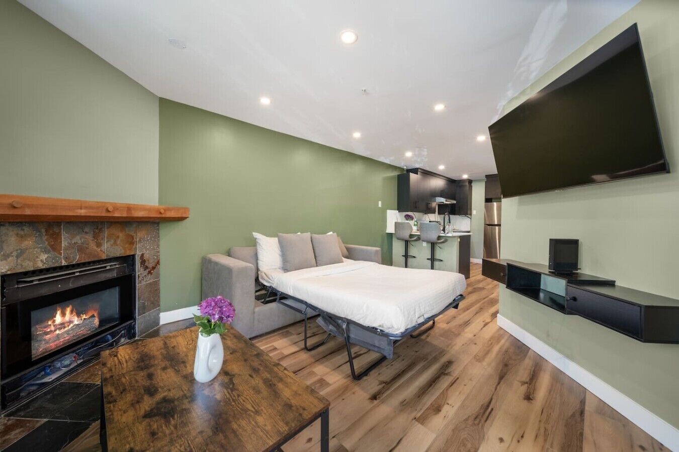 Ein modernes Schlafzimmer mit Kamin, einem Bett, einem kleinen Tisch mit einer Vase und einem an der Wand montierten Fernseher.