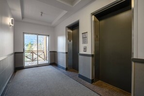 A hallway with two elevators, a door leading to an outdoor area, and a wall-mounted sign. - Whistler Central |Free PKG&Hot Tub,Walk2Everything (Whistler)