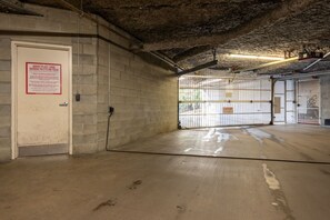 Un garage avec une porte fermée, une pancarte indiquant l’emplacement du local à ordures/à recyclage du marché, et un panneau d’avertissement sur le portail.