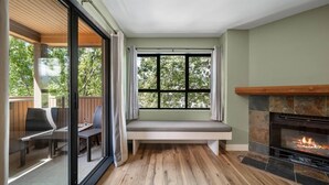 Een kamer met een open haard, een bankje onder een raam en een glazen deur die leidt naar een terras.