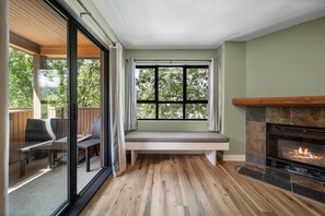 A room with a fireplace, a bench under a window, and a glass door leading to an outdoor seating area. - Whistler Central |Free PKG&Hot Tub,Walk2Everything (Whistler)