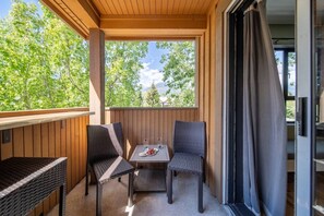 Ein Balkon mit zwei Korbstühlen, einem kleinen Tisch mit Teller und Glas sowie Blick auf Bäume und Berge.