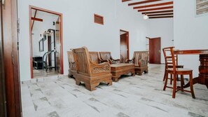 A room with a wooden sofa set, a dining table with chairs, and a mirror on the wall.