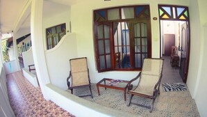 Un passadís amb una escala que condueix a una habitació amb dues cadires de vimet, una taula petita i una finestra amb un marc decoratiu.