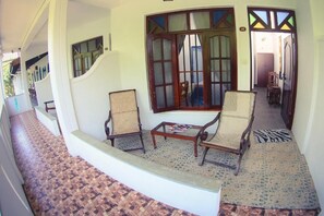 A corridor with a staircase leading to a room with two wicker chairs, a small table, and a window with a decorative frame.