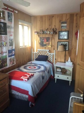 Una camera da letto con pannelli in legno, un letto con coperta a motivi, un comodino con lampada e un quadro appeso al muro.