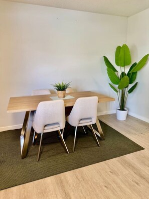 A dining area with a wooden table, two white chairs, a green plant, and a small potted plant. - Modern Cozy 2 BR Retreat Near DT & CTrain (Calgary)