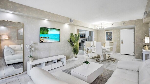A modern living room with a flat-screen TV, white sofas, a coffee table, and a dining area with a white table and chairs. - Ocean View Condo in Beachfront Resort Beach, Pool, Gym 607 (Miami)