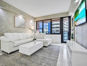 A modern living room with a sectional sofa, a coffee table, and a flat-screen TV mounted on the wall. - Ocean View Condo in Beachfront Resort Beach, Pool, Gym 607 (Miami)