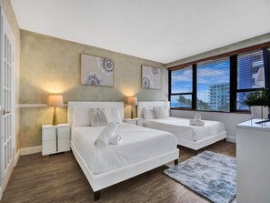 Une chambre d’hôtel avec deux lits, un bureau, une fenêtre avec des stores et des œuvres d’art accrochées au mur.