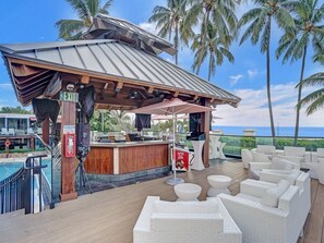 Eine Strandbar mit Pool, weißen Korbmöbeln und Blick auf den Ozean.